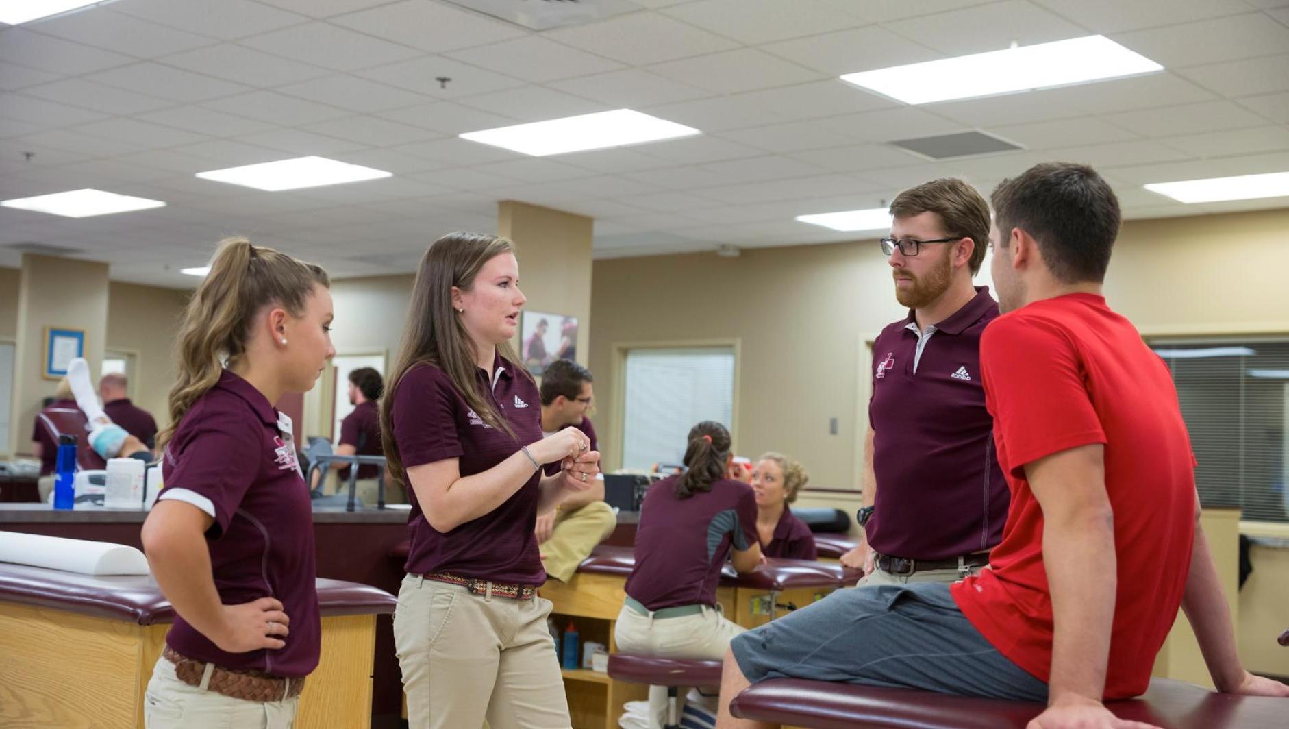 Three athletic training students consult with a client in the athletic training facility