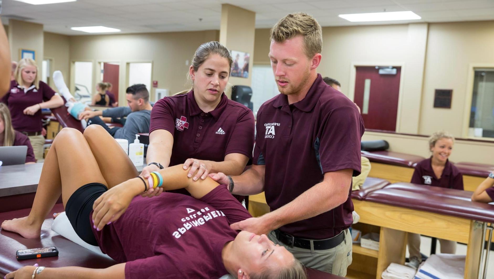 Two athletic training students perform treatment on a student-athlete's arm in the Athletic Training Facility
