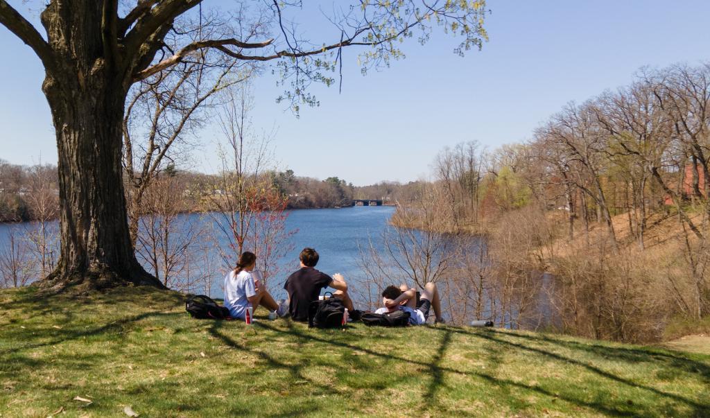 Students relax in the warm sunshine on Rally Hill overlooking Lake Massasoit at Springfield College on Thursday, April 13, 2023.